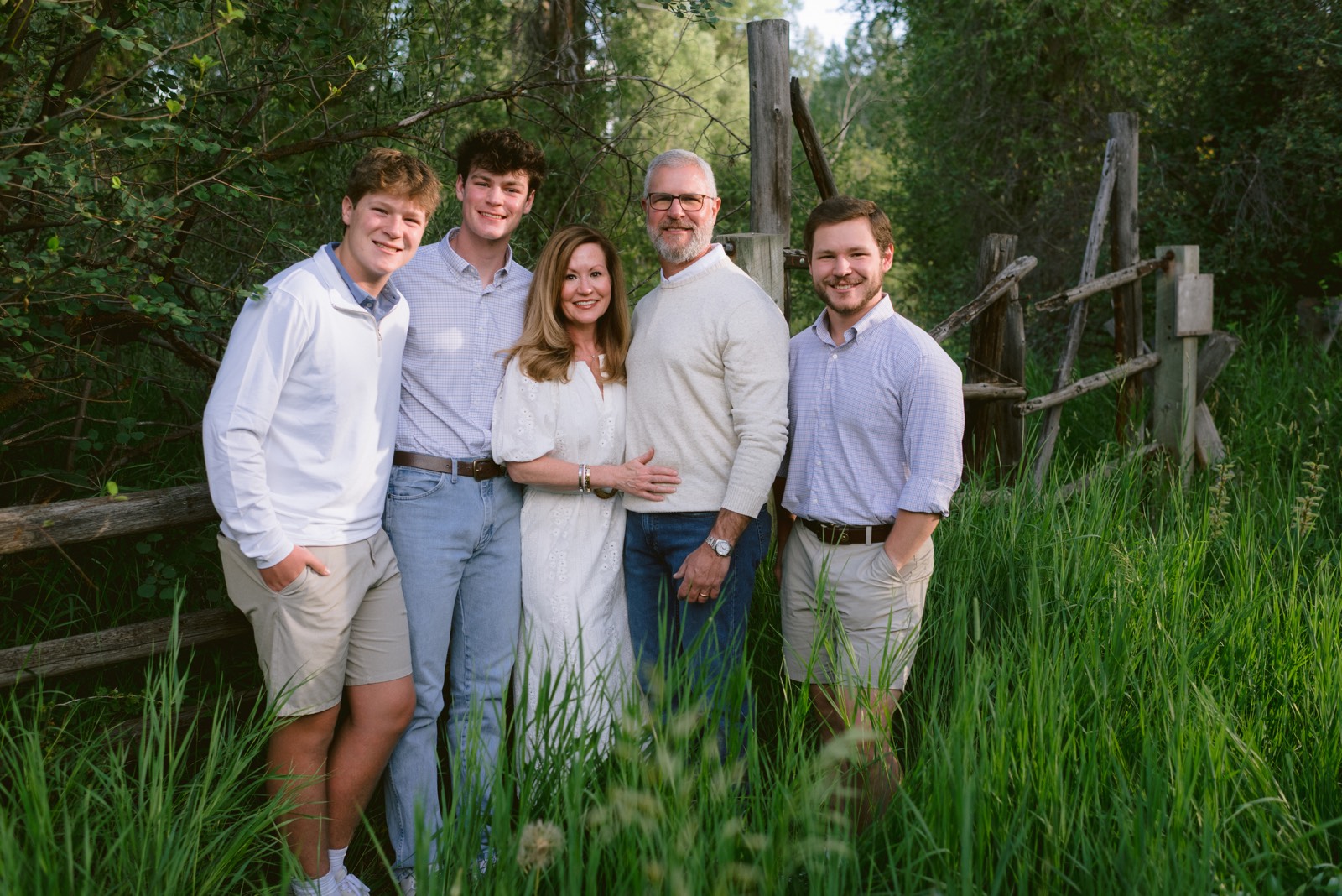 Family of five portrait in a lush green meadow by a rustic fence — Steamboat Springs family photographer Andy Barnhart